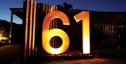 Backlit house numbers on a timber slat fence at dusk