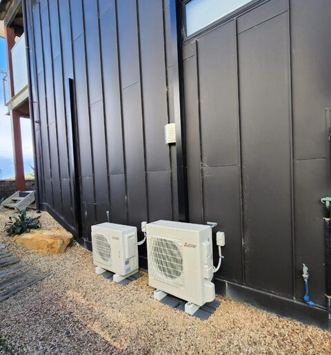 Two outdoor split system units on brackets against dark cladding