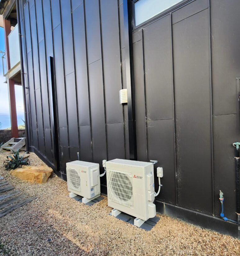 Two outdoor split system units on brackets against dark cladding